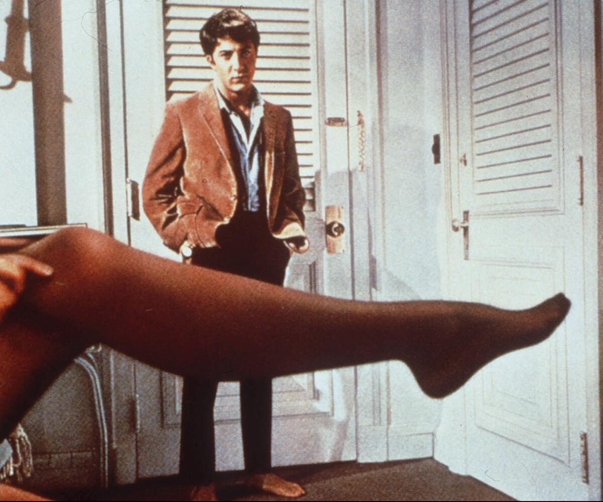 Dustin Hoffman looks over a woman's extended leg in black stockings.