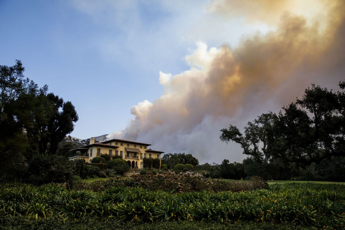 A plume of smoke from the Thomas fire rises behind a home in Montecito.