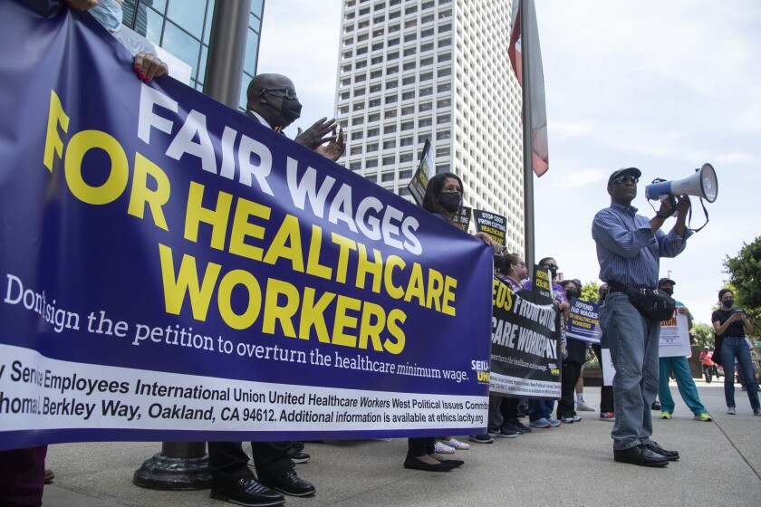 A man speaking into a bullhorn stands in front of a banner reading "Fair wages for healthcare workers"