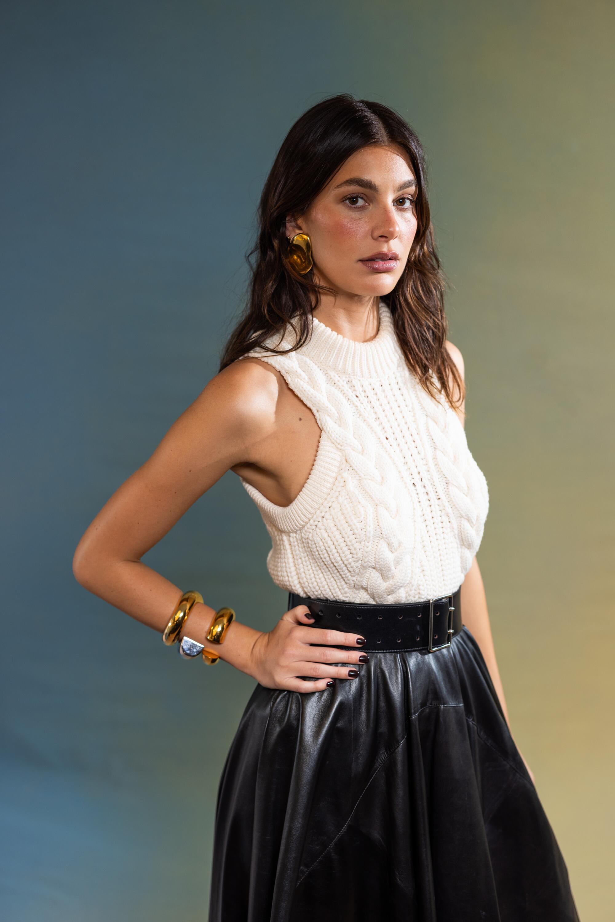 Camila Morrone in a sleeveless sweater and black skirt and a hand on her waist.