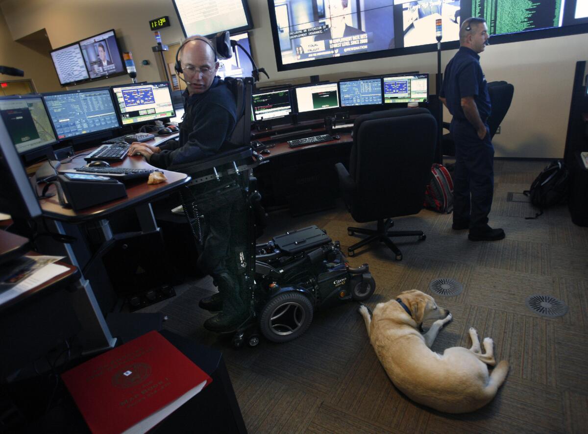 Dispatcher Mark Gilchrist stands in his specially designed wheelchair working on a call as his helper dog Calendar lies nearby.