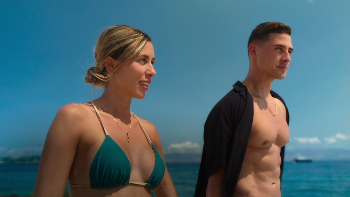 An engaged couple in swimsuits on a sunny beach.