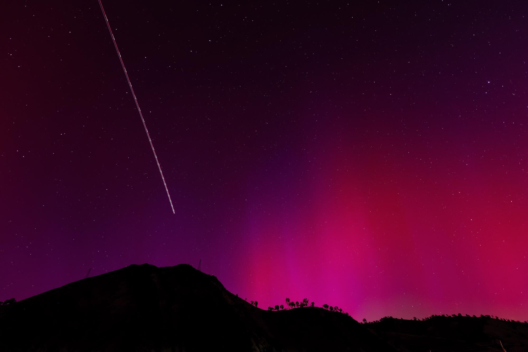 The blinking lights of a plane streak through the aurora borealis over Lake Berryessa, Calif., on May 11.