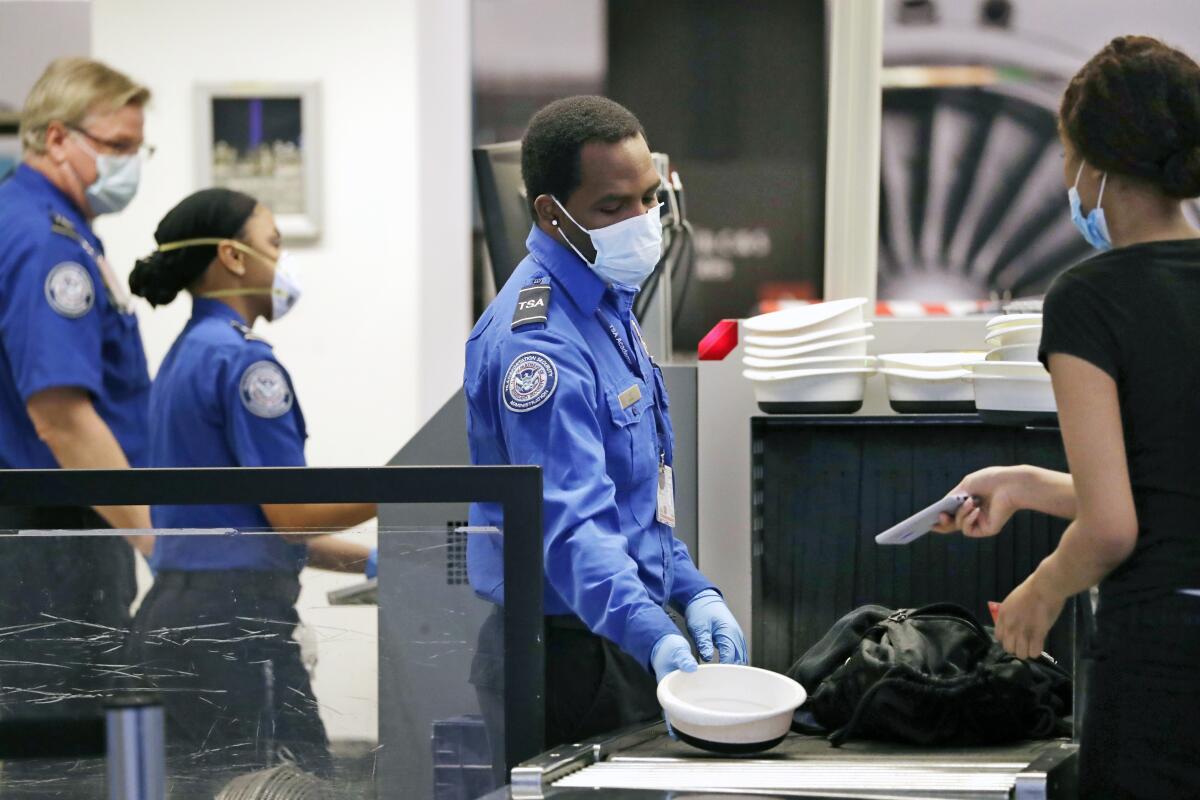 A TSA officer holds out a plastic bowl for a passenger to put her phone into at an X-ray machine