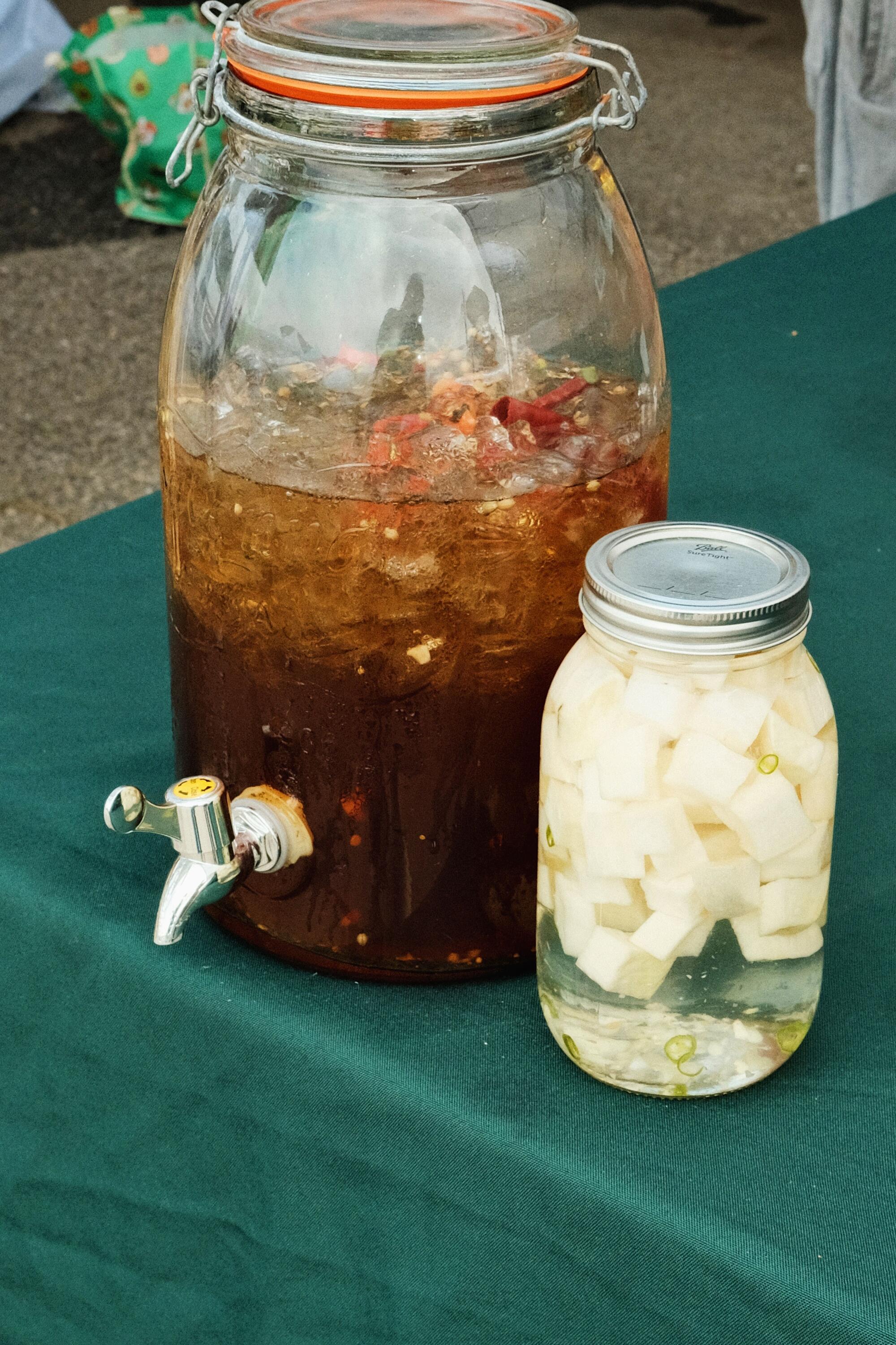 A jar of pickled white radish and a large container of iced brown pickling brine on a green tablecloth