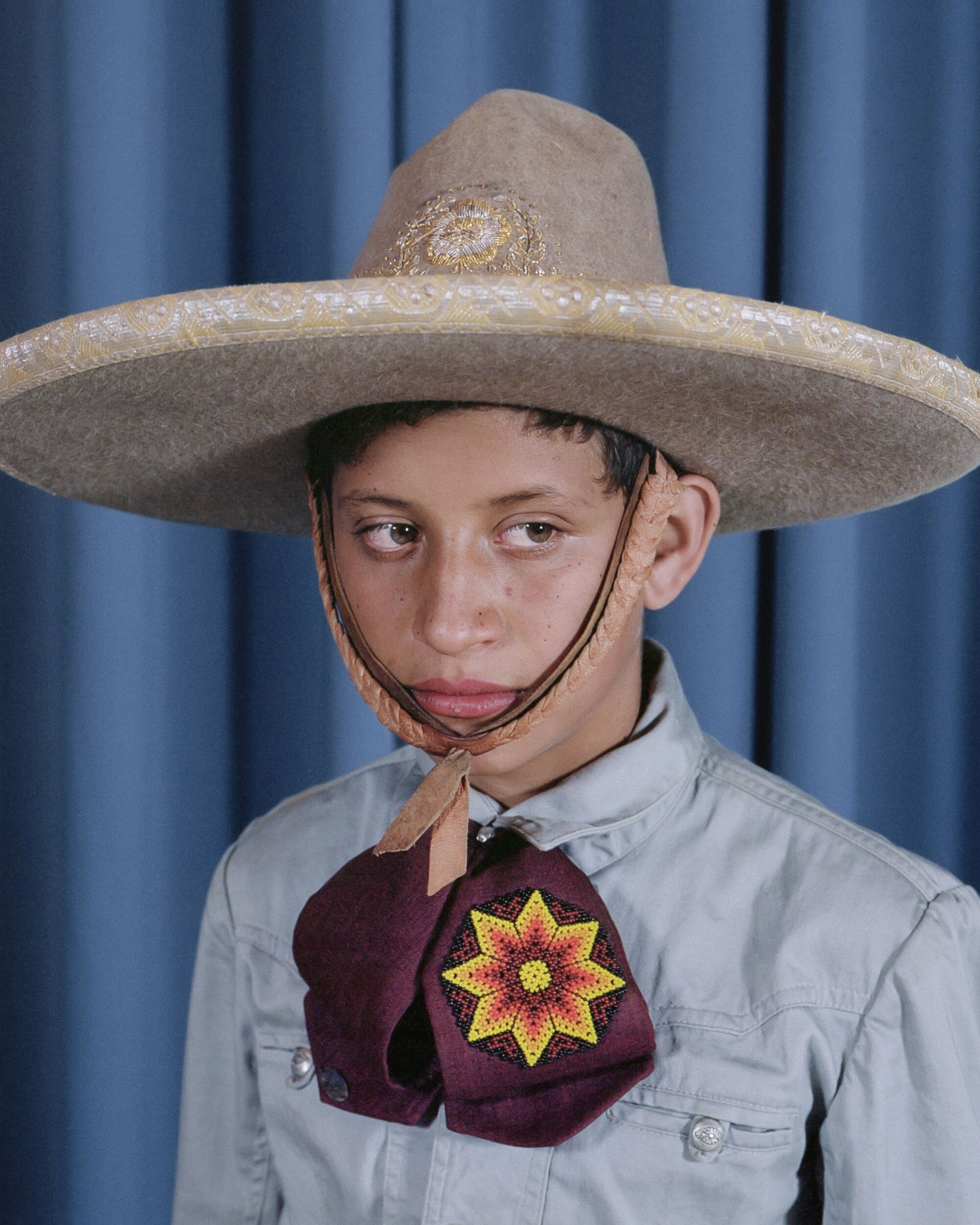 A boy in a sombrero poses for a portrait on a blue background.