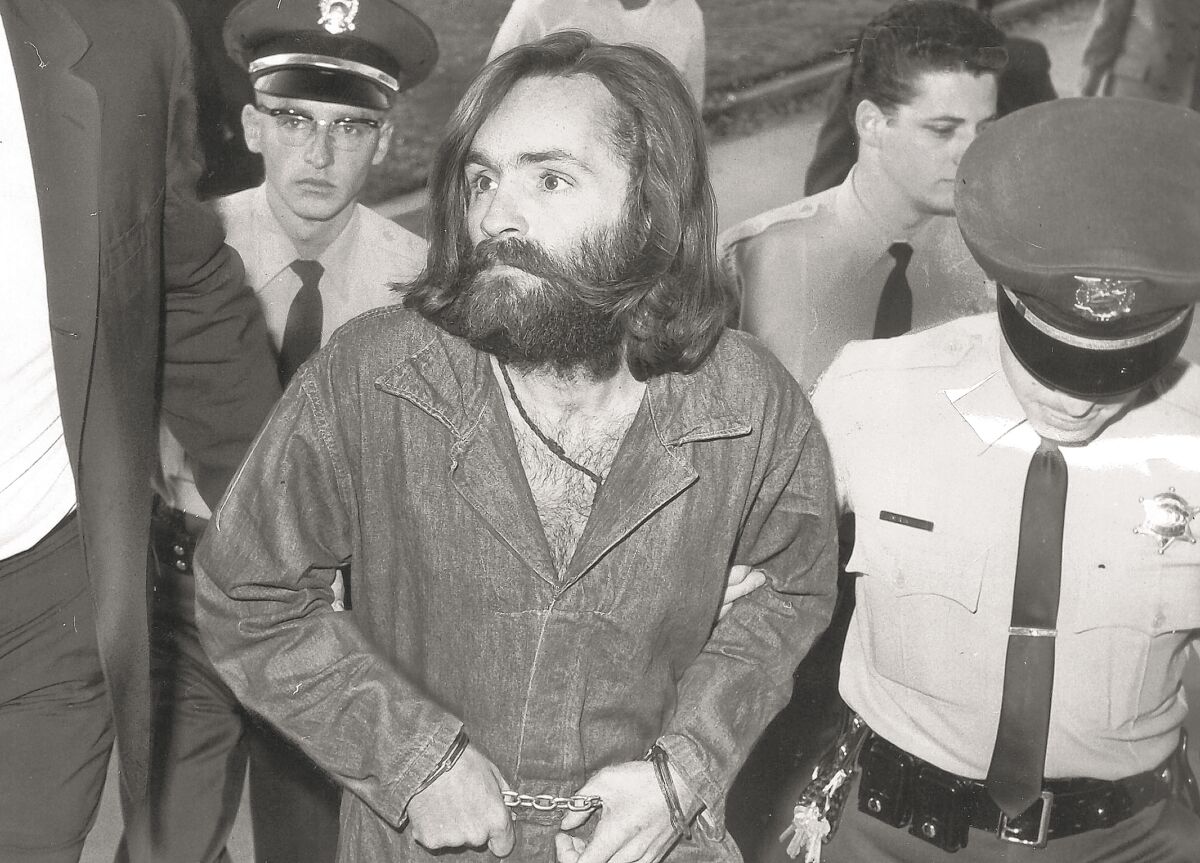 Charles Manson in handcuffs flanked by police officers