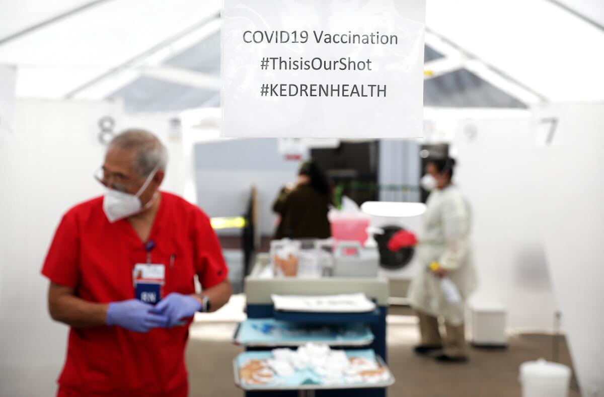 A medical technician stands in a tent at an outdoor vaccination facility