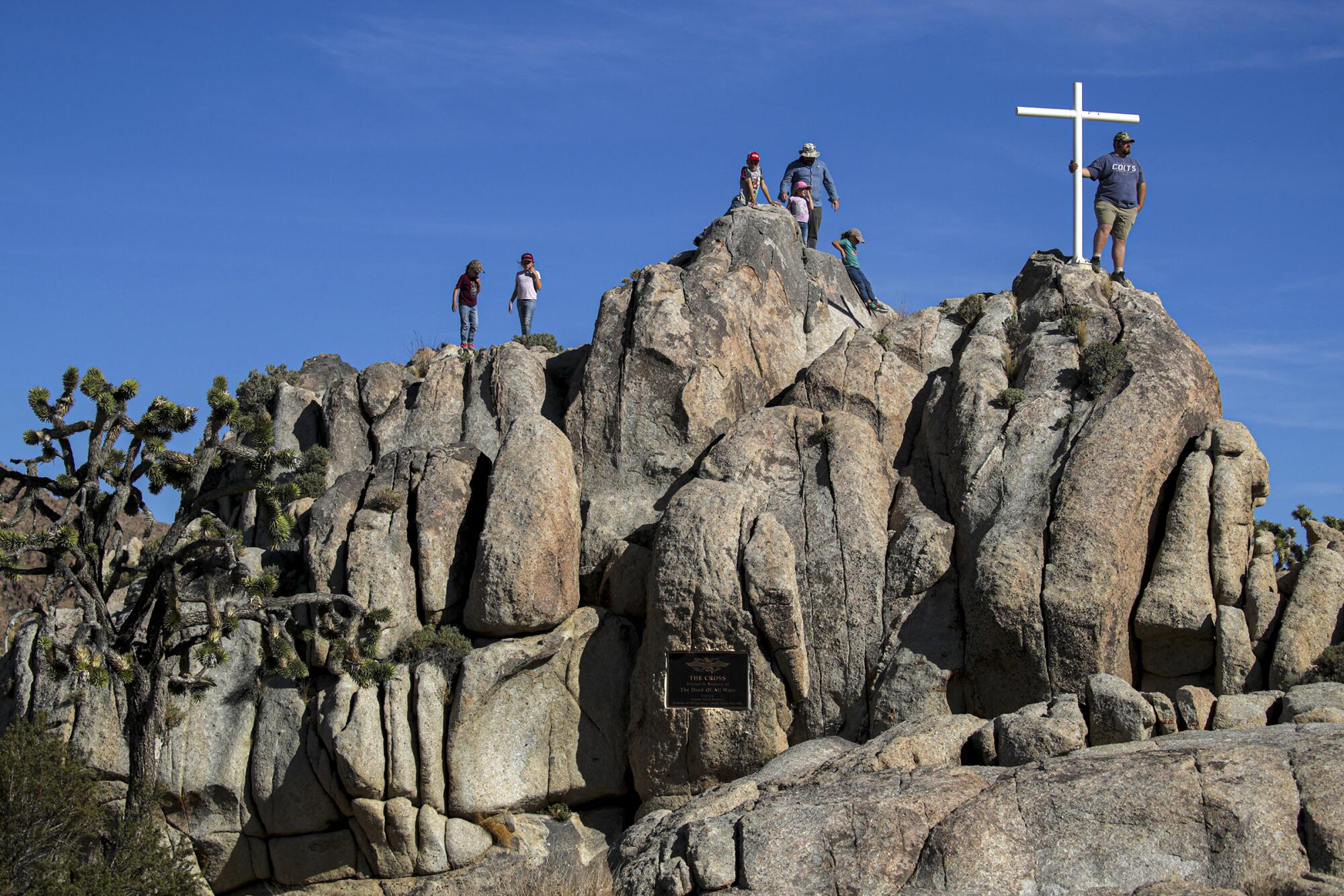 Several people stand on top of a rock formation with a cross made out of white pipes