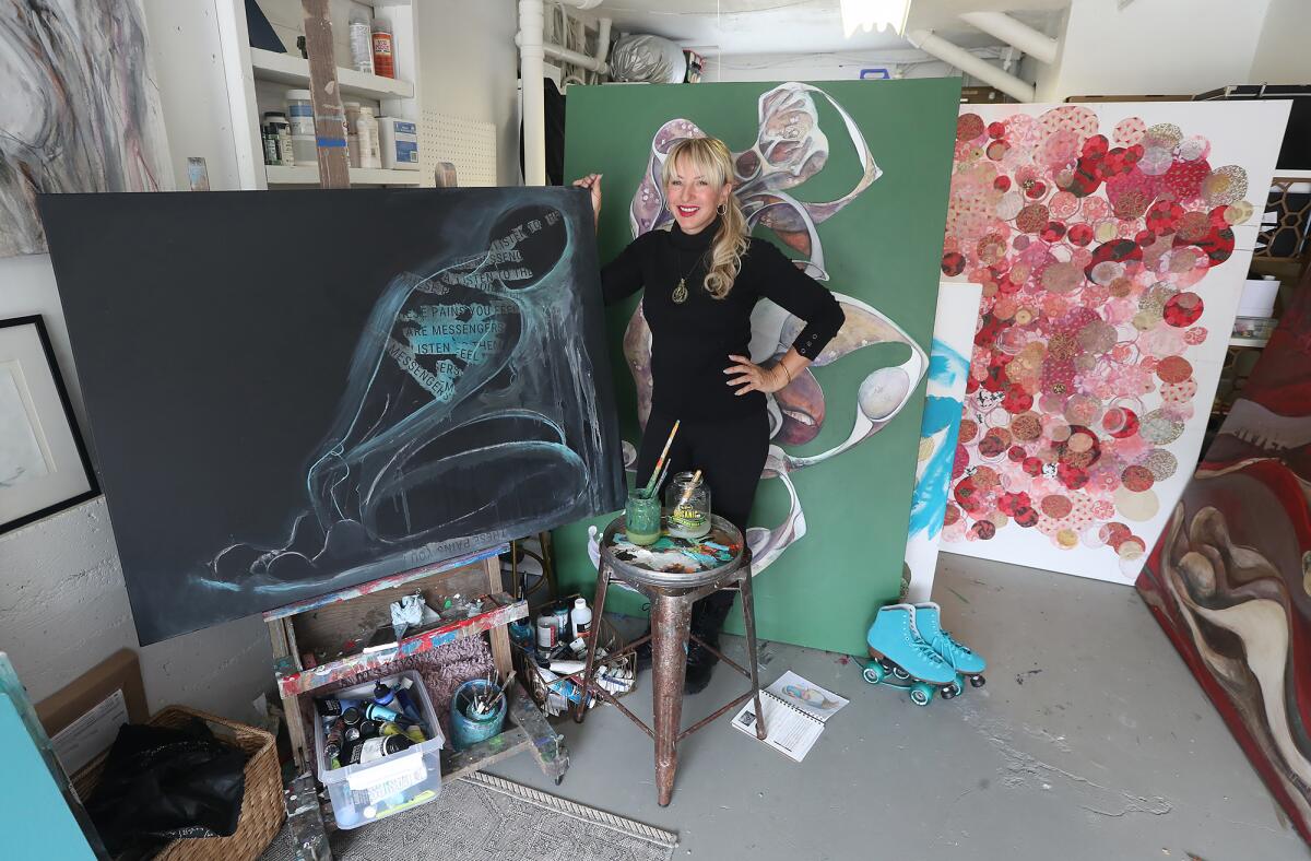 Christiana Lewis Ulwelling stands with three of her new paintings in her home studio garage in Laguna Beach.