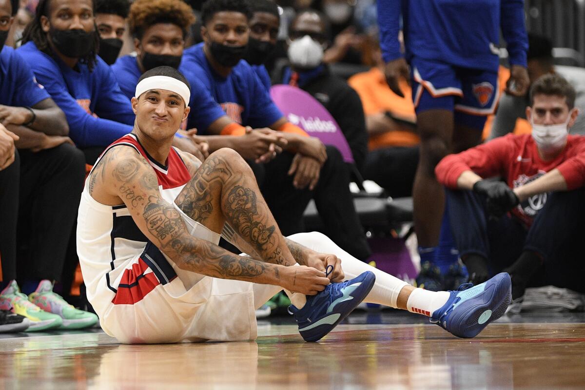 Washington Wizards forward Kyle Kuzma scrunches his face while sitting on the court and tying his shoe.