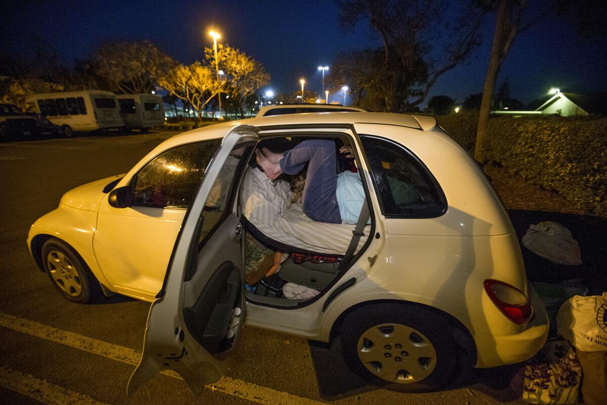 Russell awkwardly climbs through the back door of her car to sleep in the parking lot of the Carlsbad Senior Center.