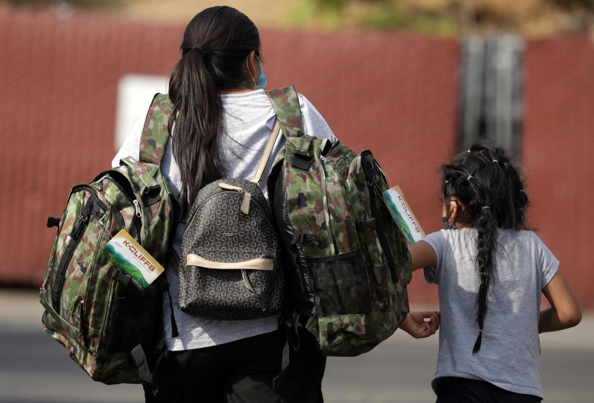Women and little girl walking away with school backpacks.