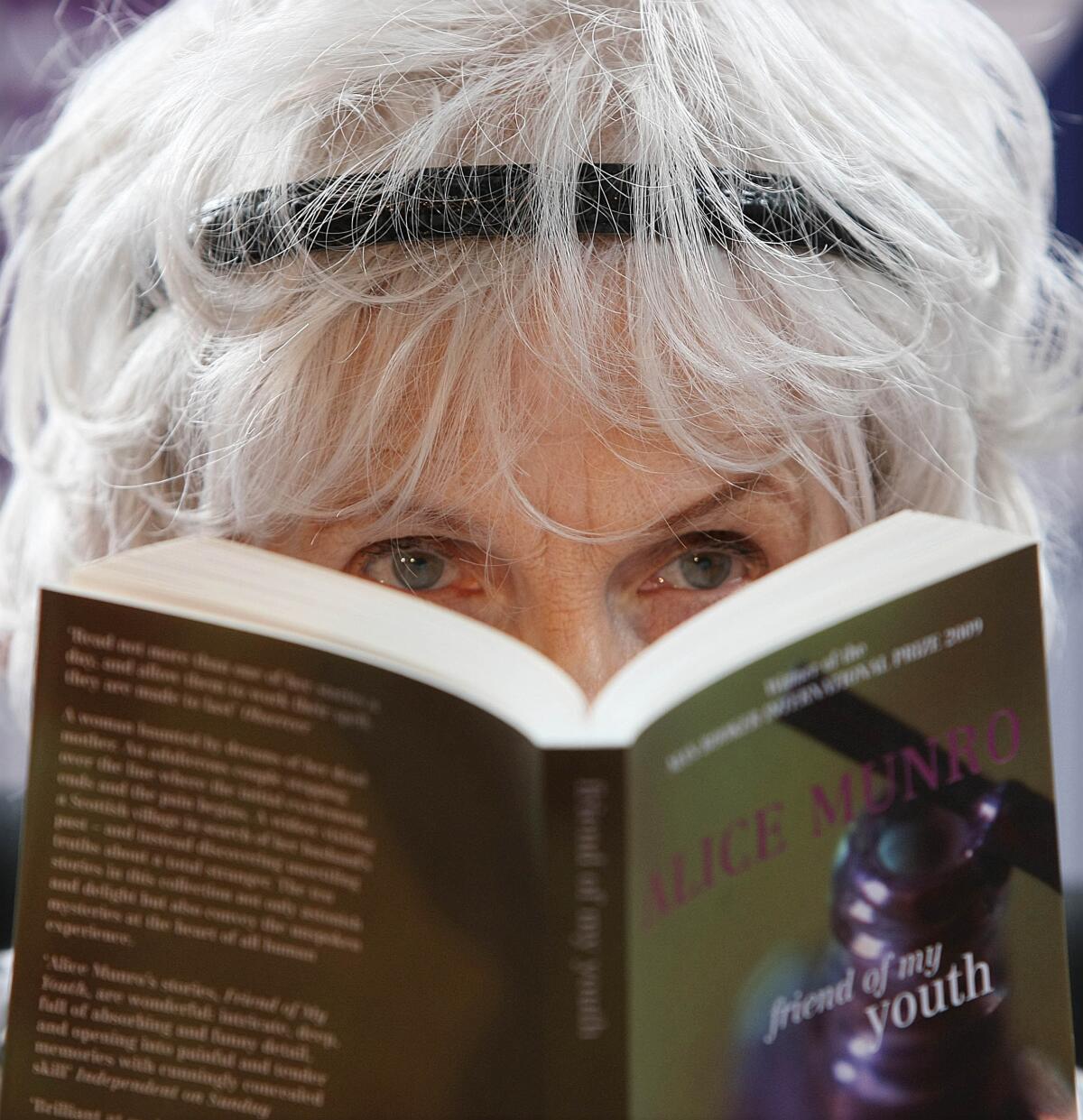 Alice Munro holding an open book and looking over it