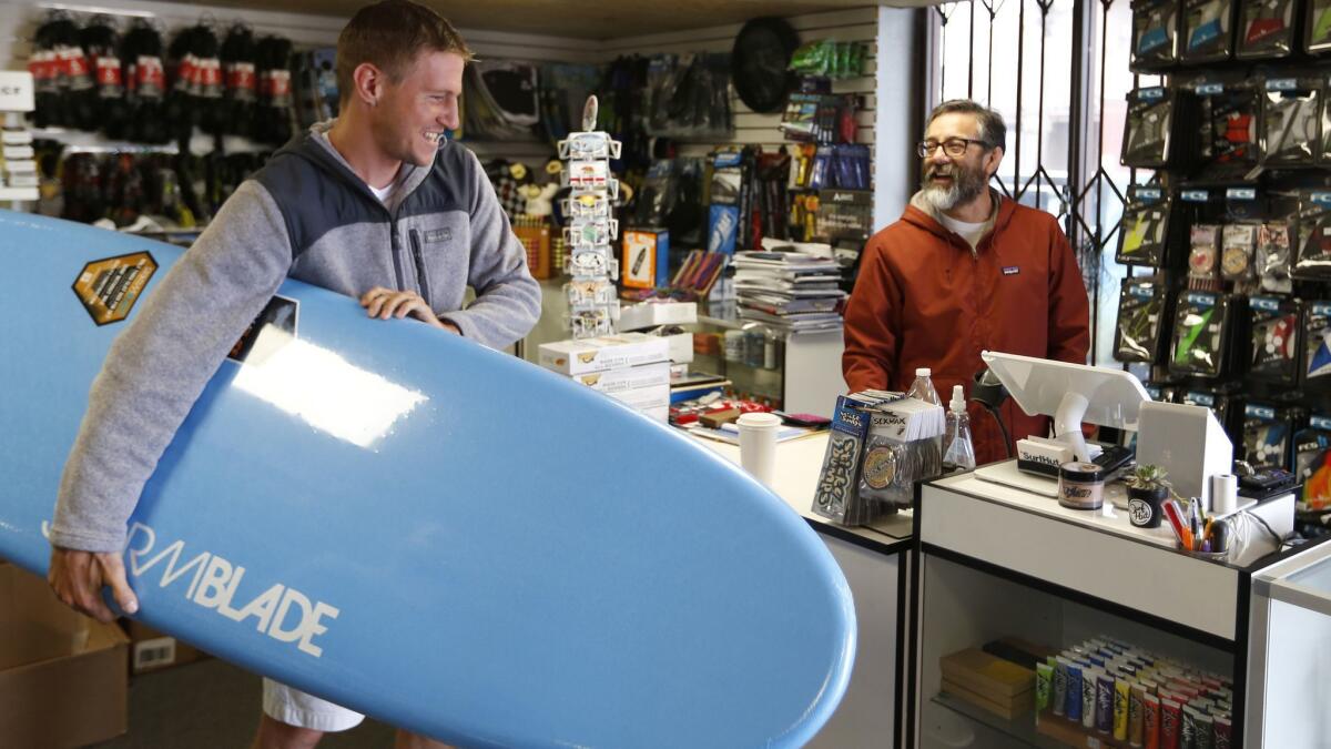 Jesse Ramirez, right, owner of the Surf Hut in Imperial Beach, helps customer Chris Kramer.