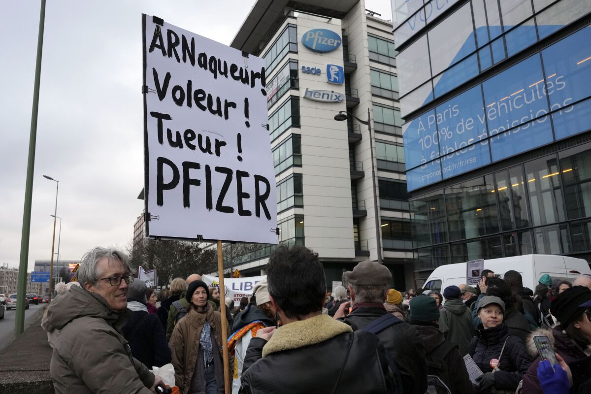 FILE - A demonstrator holds a placard reading "Scammer, thief, killer, Pfizer" during a protest against the vaccine pass and vaccinations to protect against COVID-19 in front of the Pfizer headquarters, in Paris, on Jan. 29, 2022. An anti-vaccine group that has harassed doctors and public officials in Italy and France is still active on platforms like Facebook despite efforts to rein in their abuse and misinformation. The organization, known as V_V, bombards its victims with dozens, hundreds or even thousands of abusive posts. (AP Photo/Thibault Camus, File)