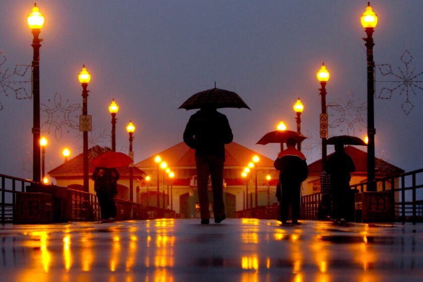 People stroll with their umbrellas on the Huntington Beach Pier during rain -- something that didn't occur too often in Southern California during an El Niño year.
