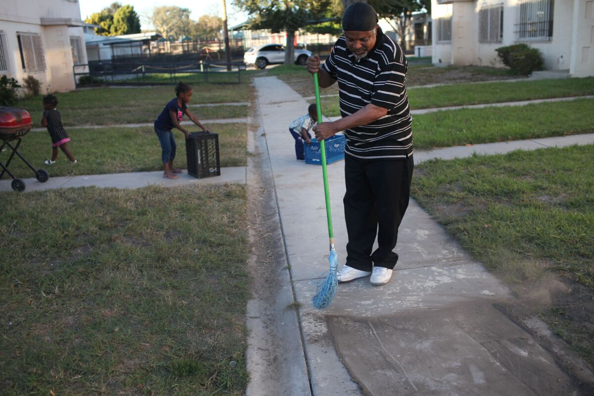 Craig McGruder sweeps the sidewalk leading to his sons' home in the Jordan Downs housing complex in Watts.