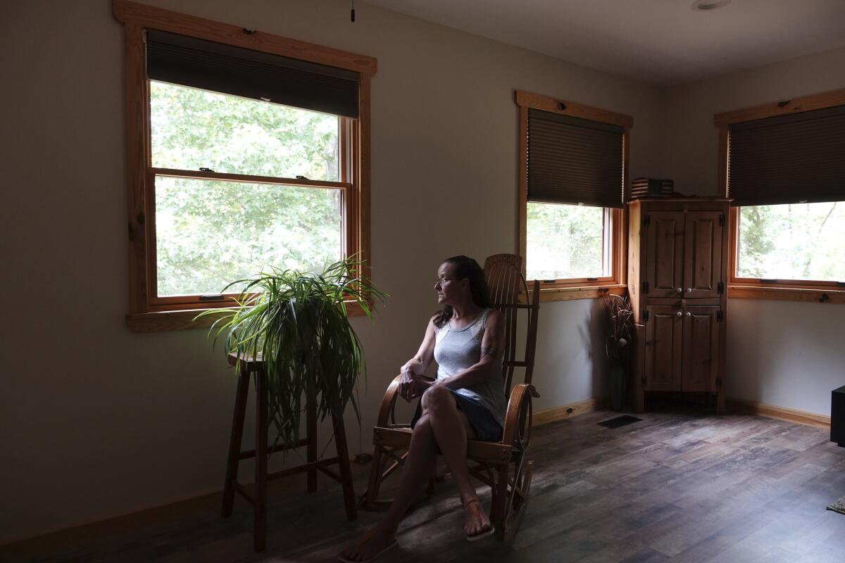 A woman sits near a window in a shadowy room.