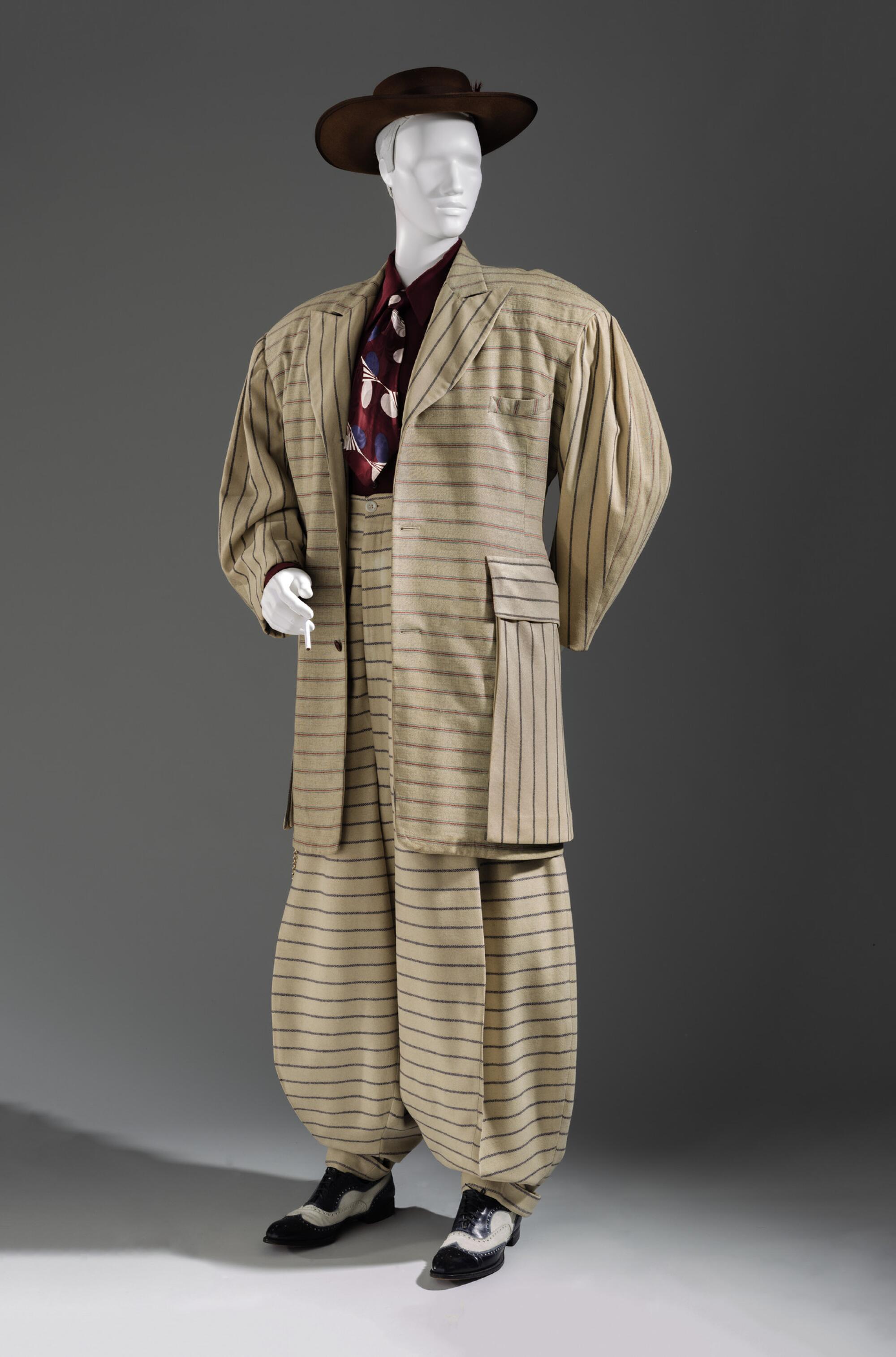 A mannequin dons a flamboyant pale yellow zoot suit with horizontal stripes and a burgundy shirt and tie.