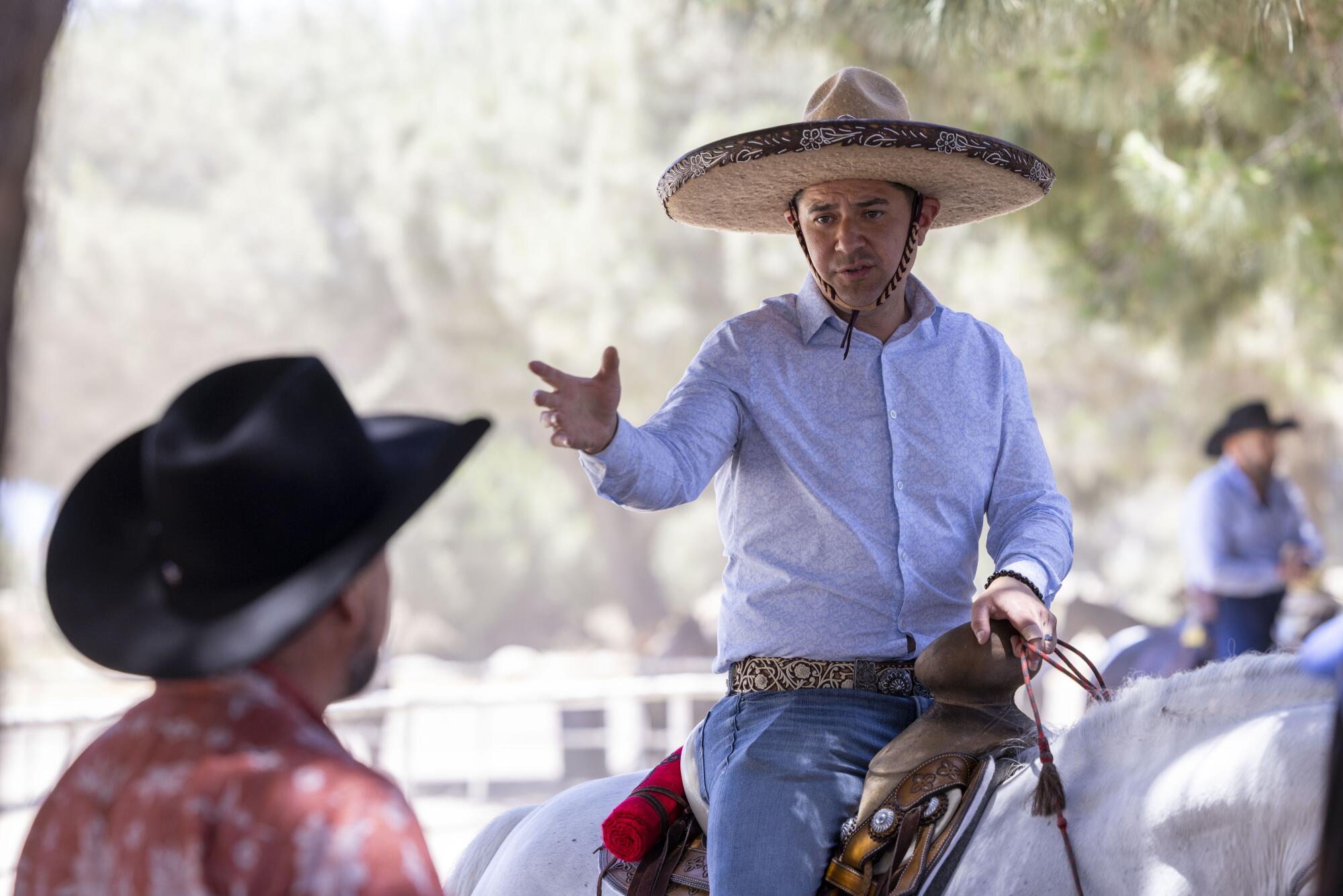A man in a sombrero sits on a horse while talking to a man in a cowboy hat.