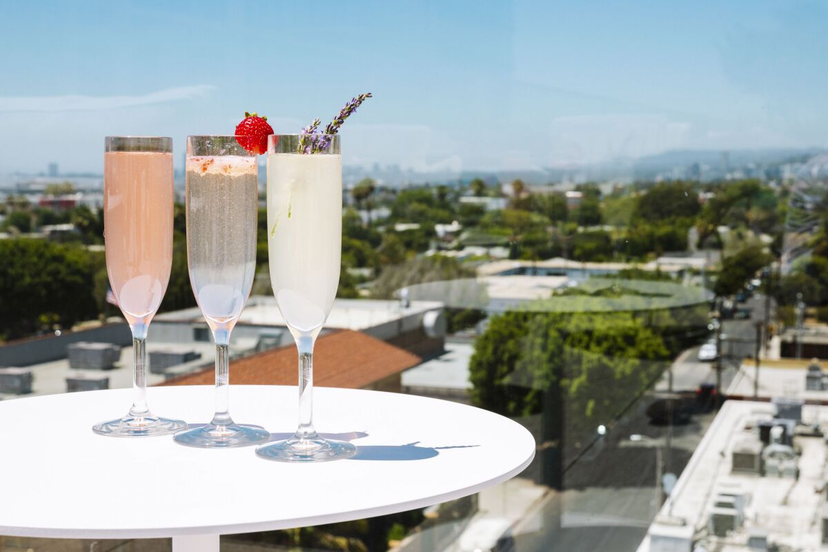 three cocktails in flute glasses on a high table on a rooftop, with Los Angeles spreading out in the distance