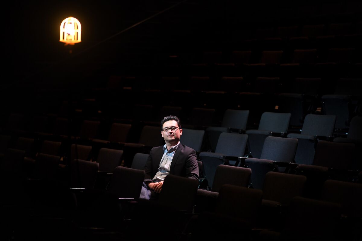 Edgar Miramontes, wearing a light blue shirt and dark jacket, sits in the auditorium of an empty theater.