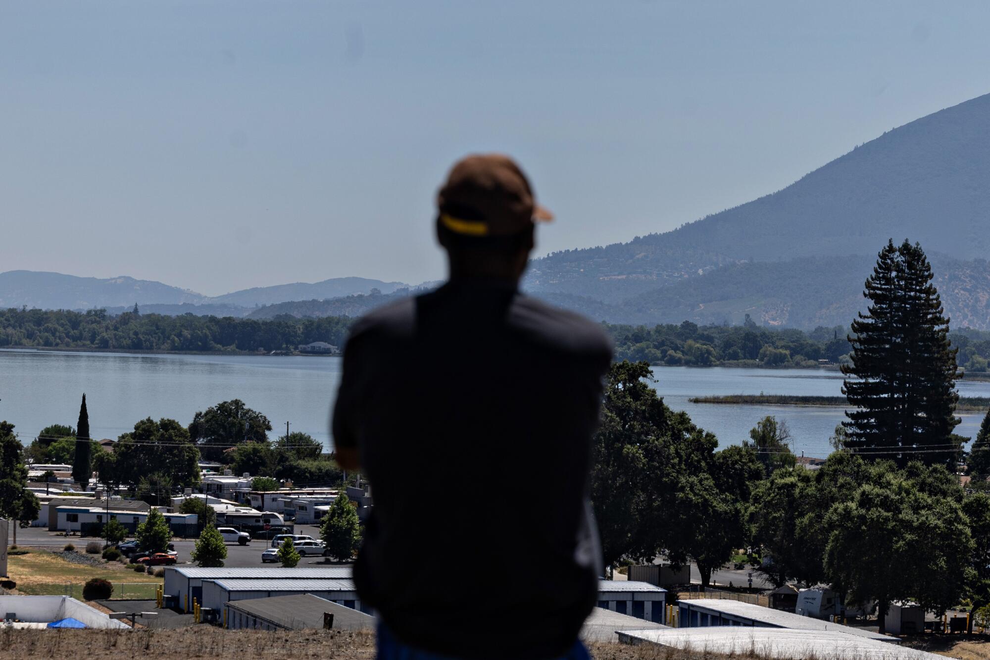 A person wearing a baseball cap looks at a lake. 