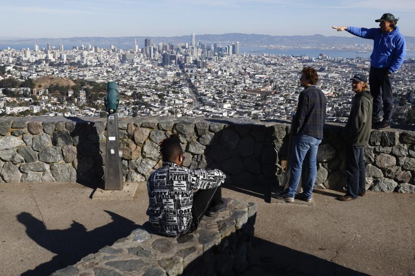 Tourists look out onto the city skyline from Christmas Tree Point on top of Twin Peaks in San Francisco, Thursday, Dec. 15, 2022. (Jessica Christian/San Francisco Chronicle via AP)