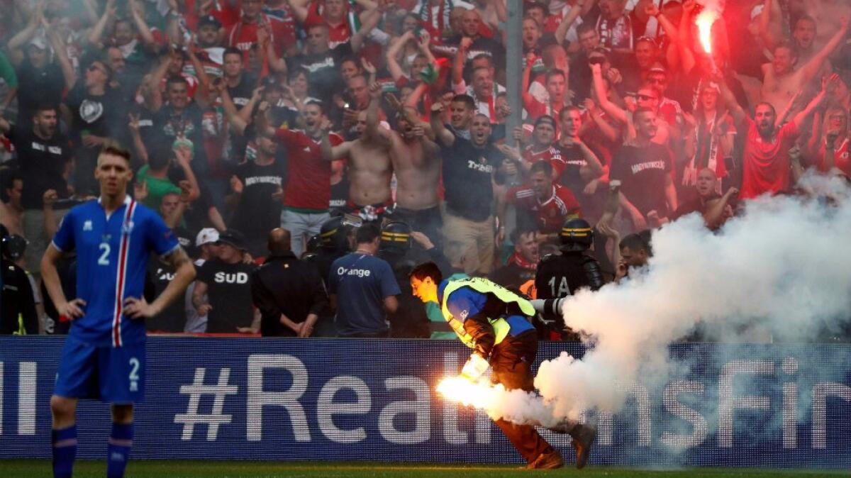 A volunteer takes a flare thrown by Hungary supporters away from the pitch during a match against Iceland on June 18.