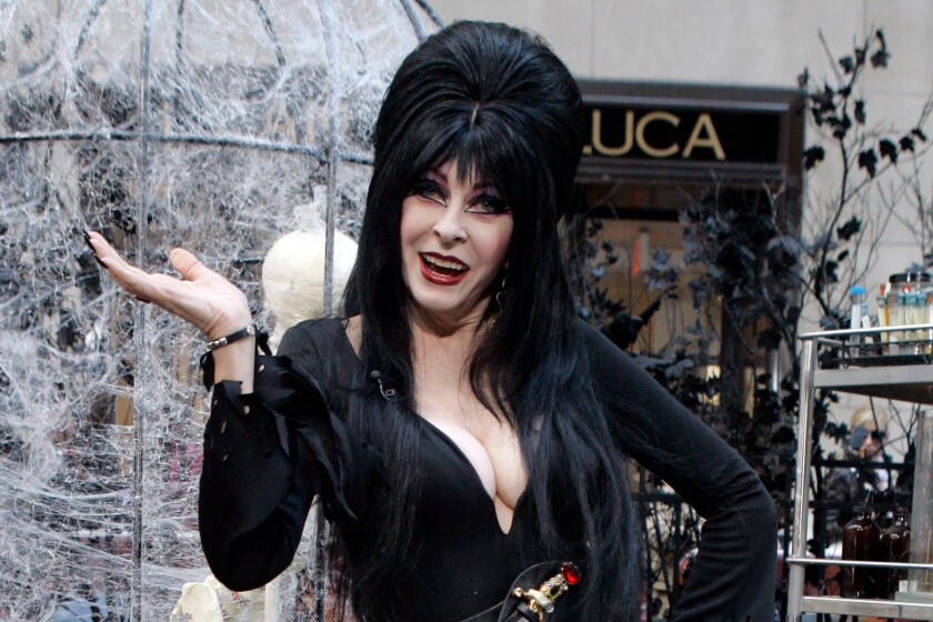 A woman with long black hair and dark eye makeup posing in a black dress