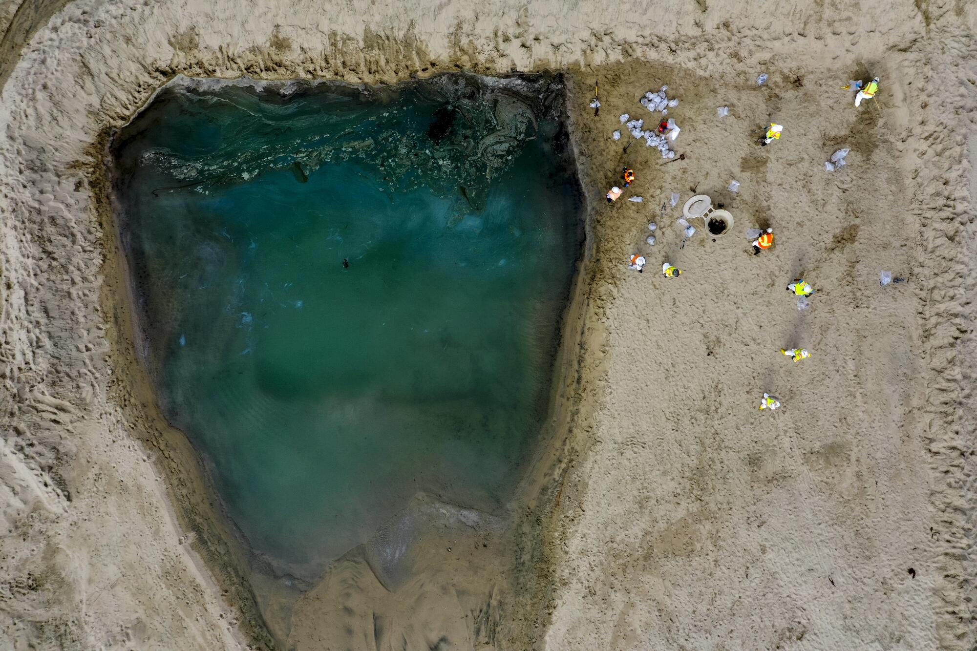 An aerial view of people gathered near the edge of a blue-green body of water surrounded by sand