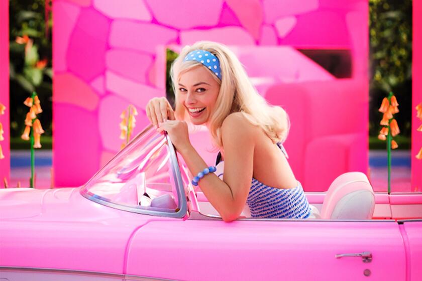 Margot Robbie with blonde hair in a blue outfit driving a pink convertible car