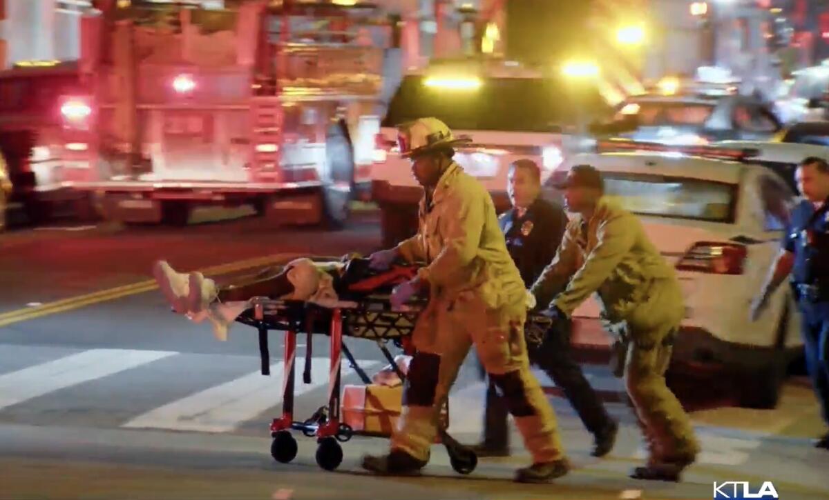 First responders wheel a gurney across a street at night near emergency vehicles.
