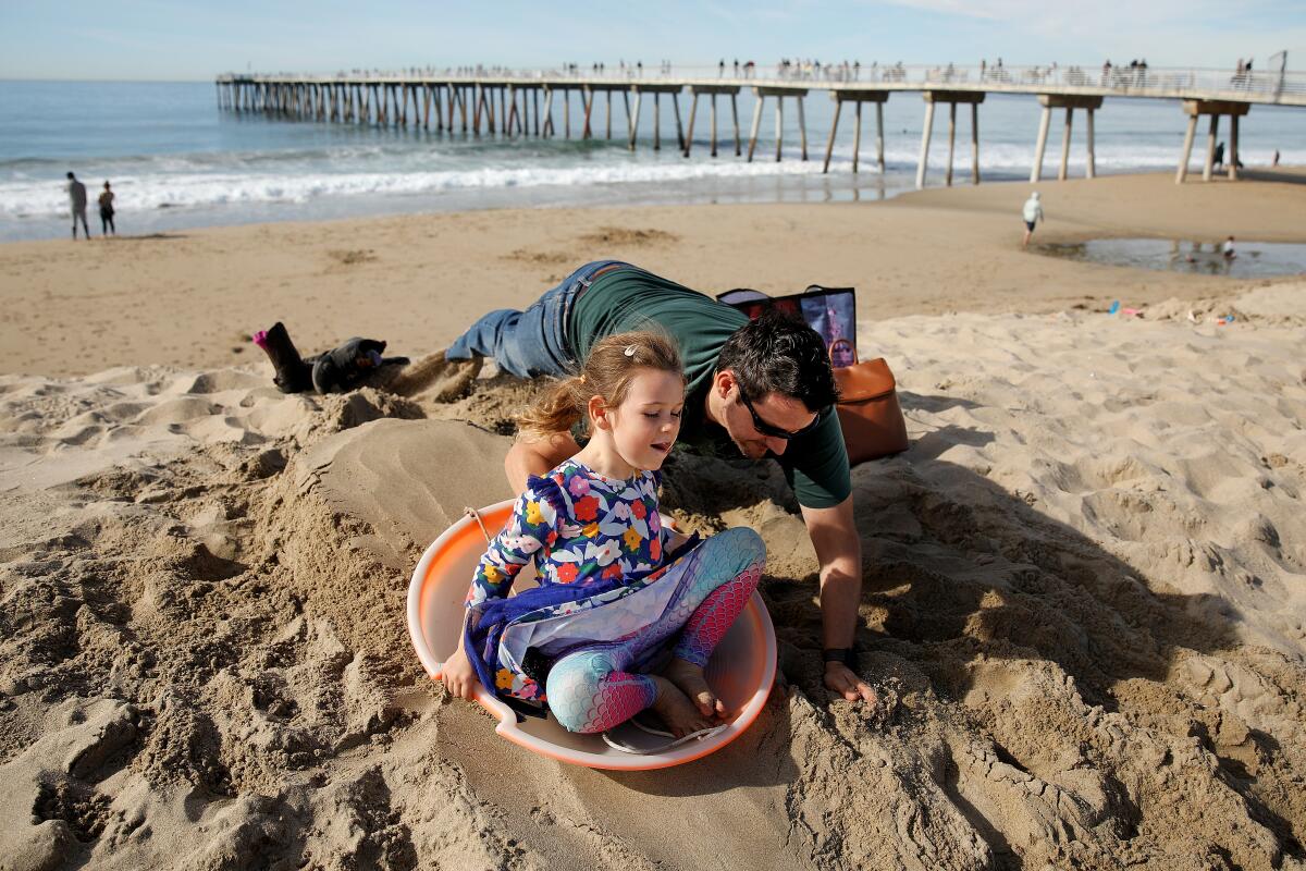 A father pushes his daughter down a hill of sand on Sunday, Dec. 25, 2022 in Hermosa Beach.
