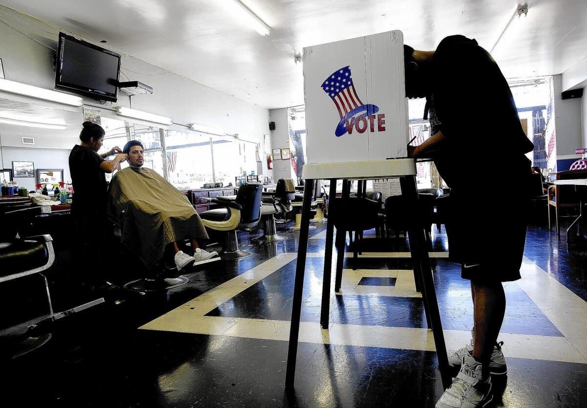 Lasbia Batista, left, gives a haircut to Jose Bejarano as Marco Garcia casts his ballot during election day at Utah's Barber Shop in Long Beach.