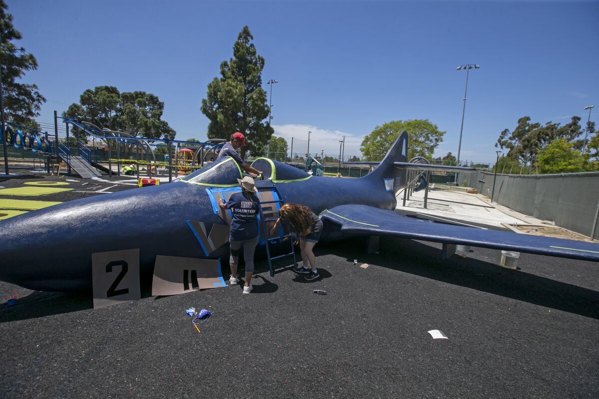 Three people check on an small airplane at a playground.