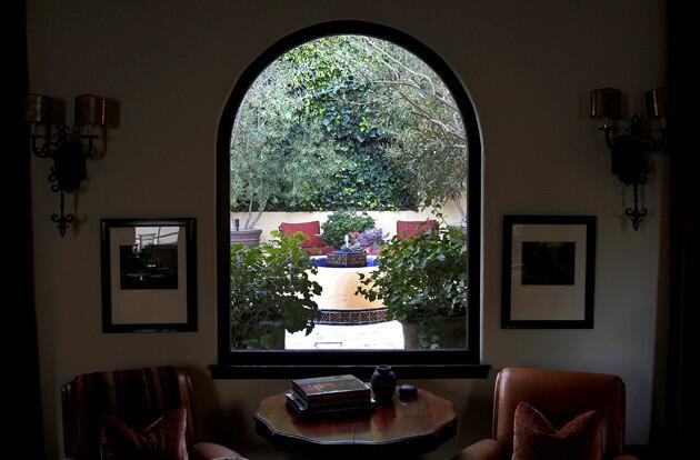 The living room's arched window provides a view of the quatrefoil fountain against a green backdrop throughout the day or, thanks to outdoor lighting, at night.
