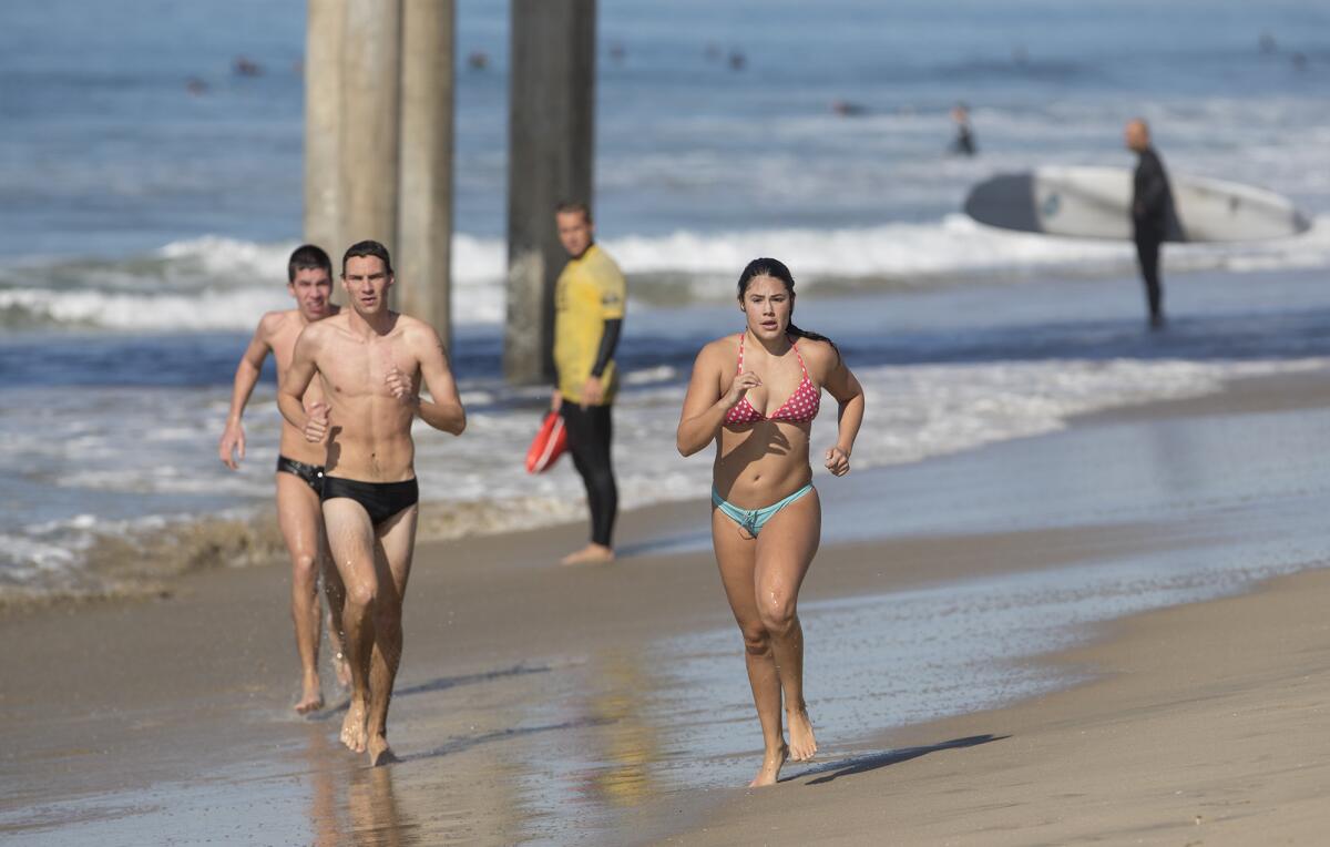 Participants run on the beach following an ocean swim during Huntington Beach lifeguard tryouts in 2018. This year's tryouts are Saturday.