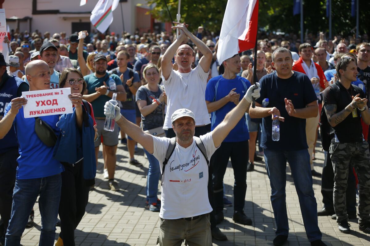 Workers with old Belarus national flags, one of them holds a poster reads "Requirement # 1 Go away!" gather during a rally at the Minsk Motor Plant in Minsk, Belarus, Monday, Aug. 17, 2020. Some thousands of factory workers have taken to the streets of Minsk demanding the resignation of Belarus' authoritarian President Alexander Lukashenko. (AP Photo/Sergei Grits)