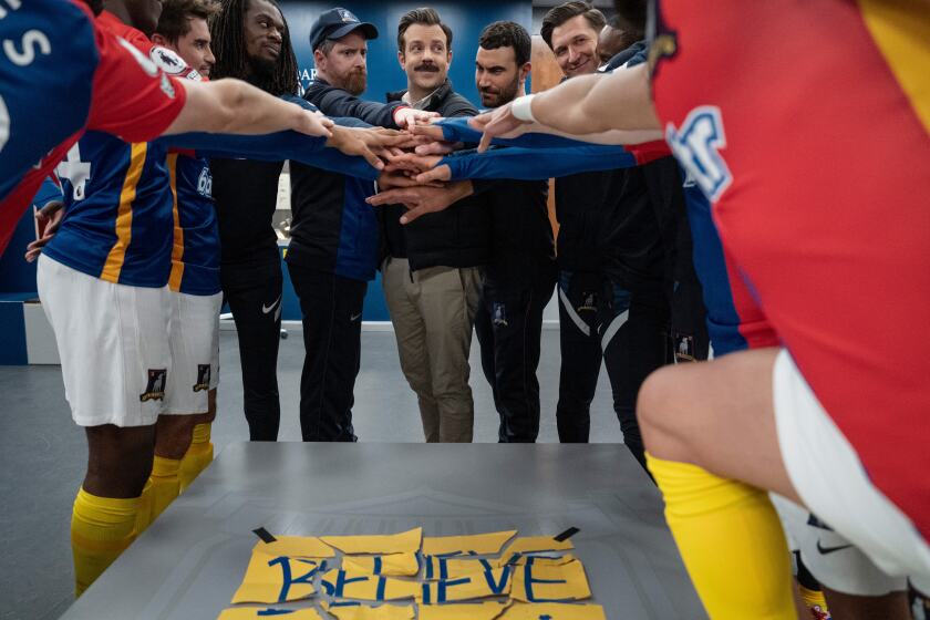 A soccer team puts hands in over a torn up, taped-together sign that says "Believe."