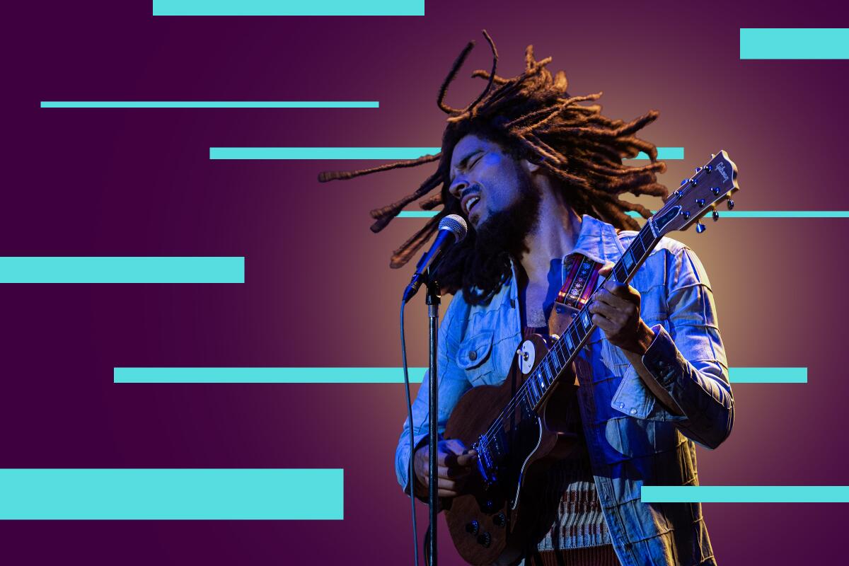 A man with dreadlocks sings into a microphone while playing guitar.