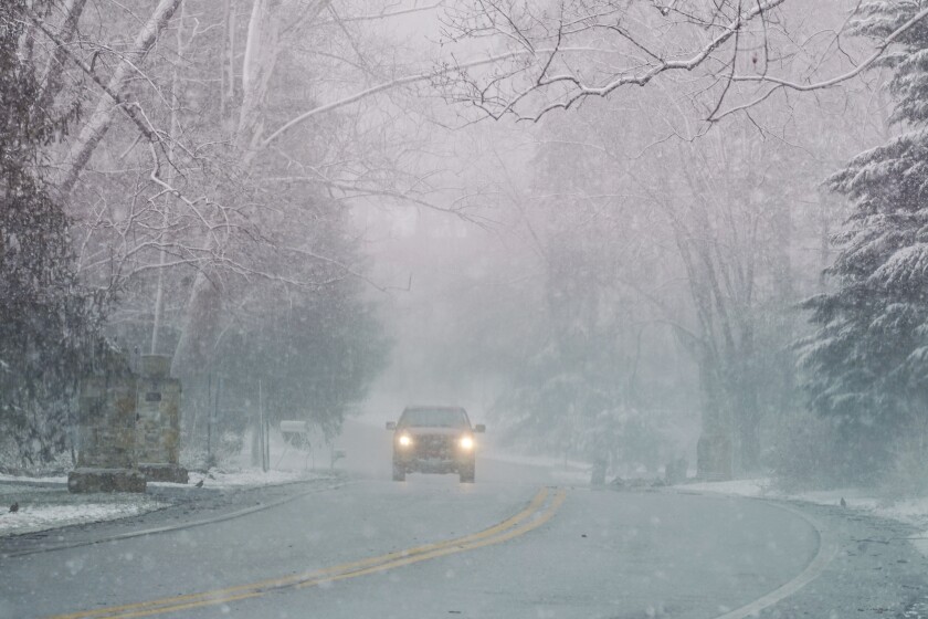 Una camioneta transita por una calle bajo la niebla y una ligera nevada 