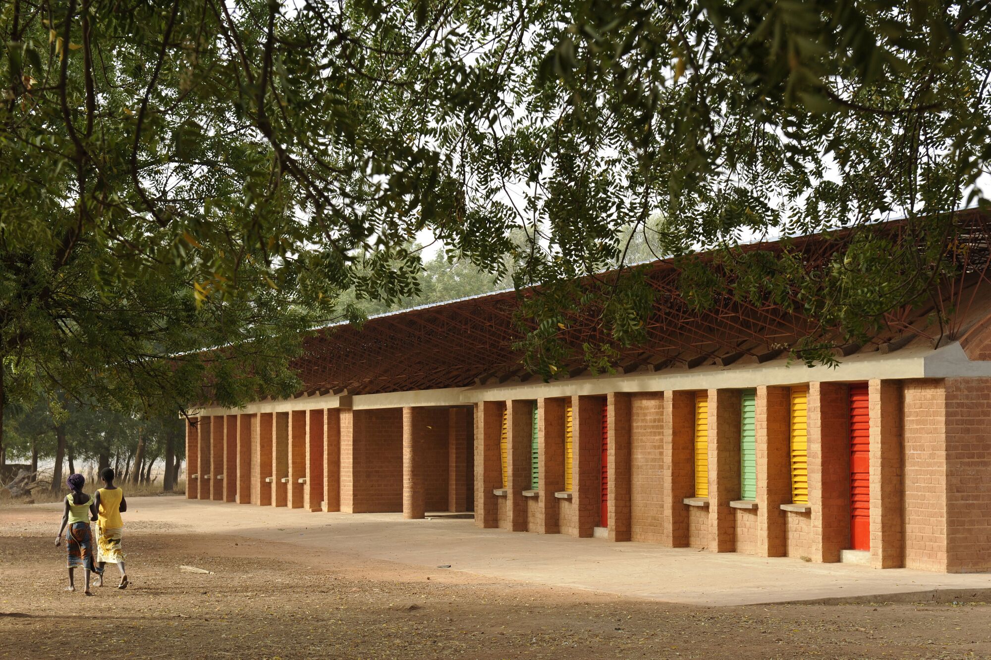 Two people walk past a low-slung horizontal building studded with bright louvered shades.