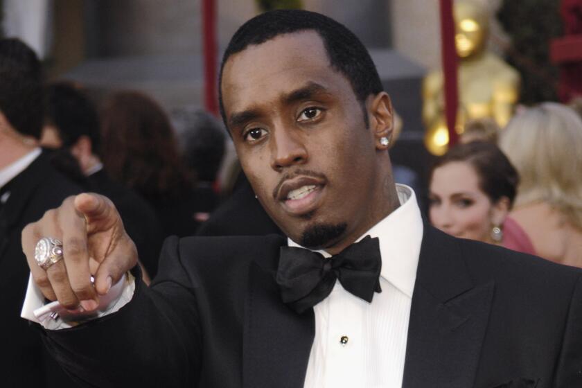 Sean "Diddy" Combs wearing a tuxedo. He points his right hand, which has a large ring, out in front of him