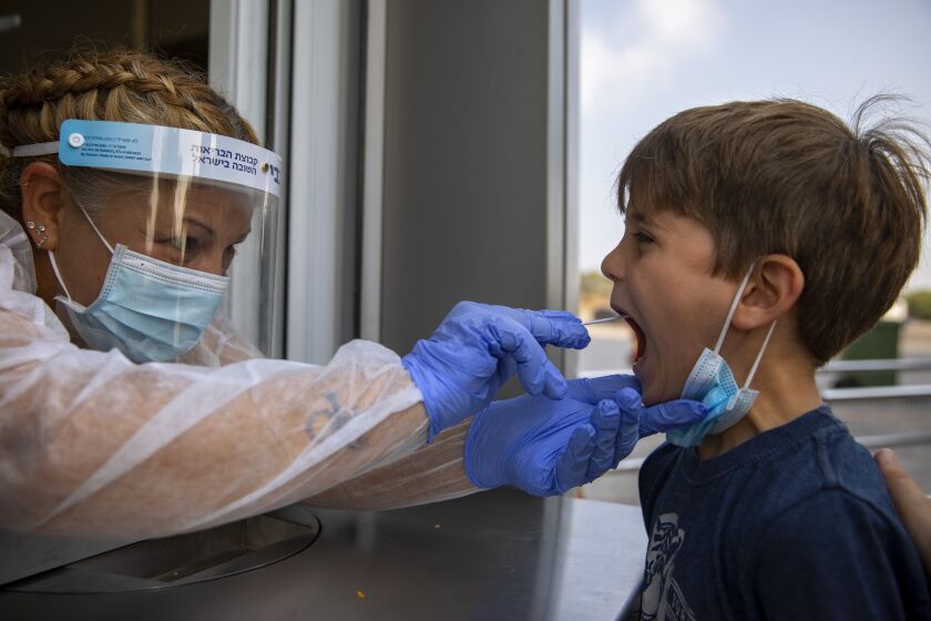 A health worker collects a swab sample from a kid to test for COVID-19, at a coronavirus testing center, in Tel Aviv, Israel.