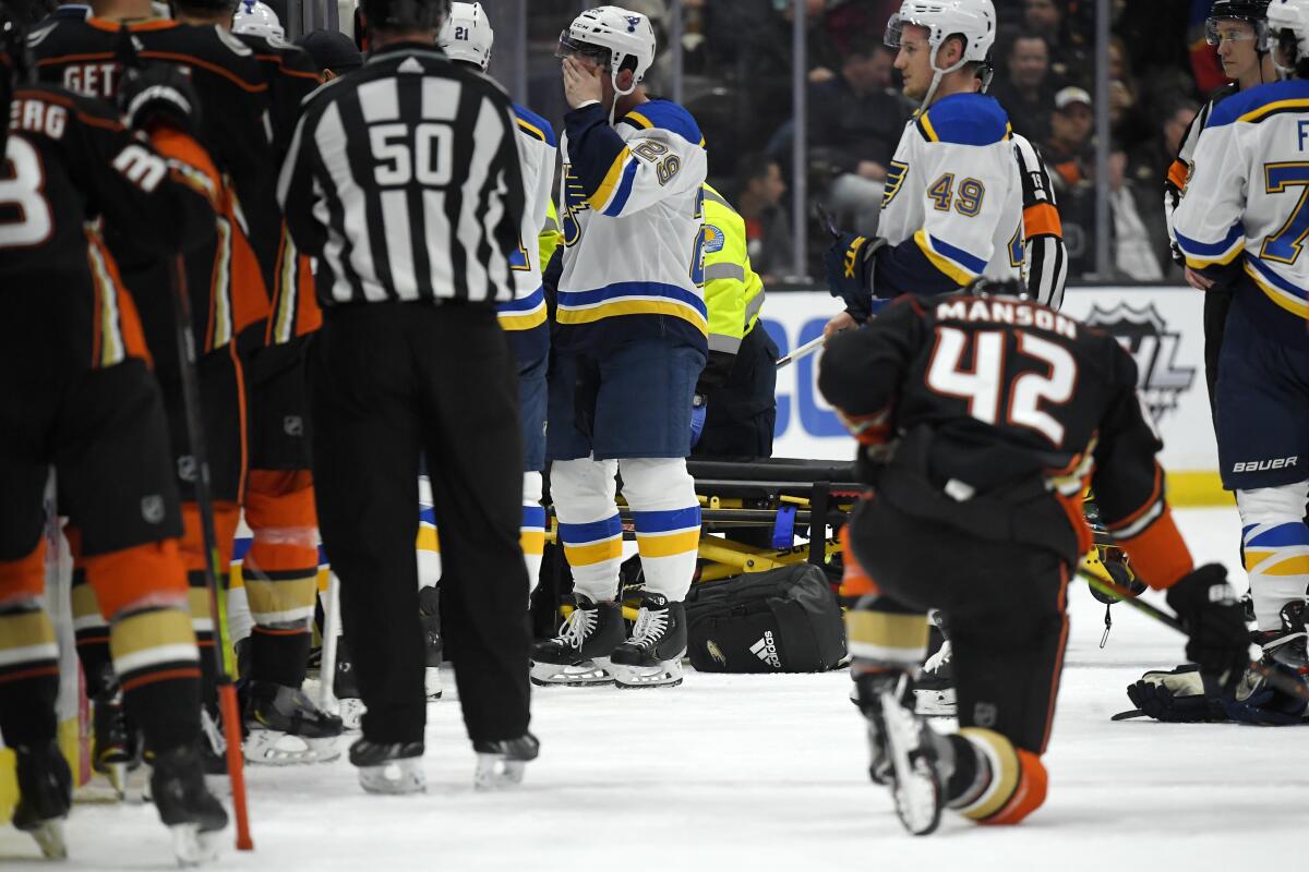 St. Louis Blues defenseman Vince Dunn, left, wipes his faces as Ducks defenseman Josh Manson kneels on the ice while medical personnel work on Blues defenseman Jay Bouwmeester.