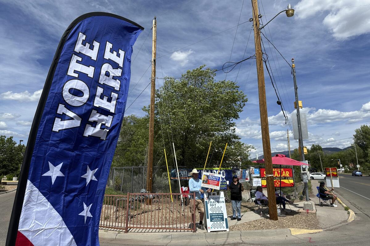 A "vote here" banner on a street corner on a sunny day. 