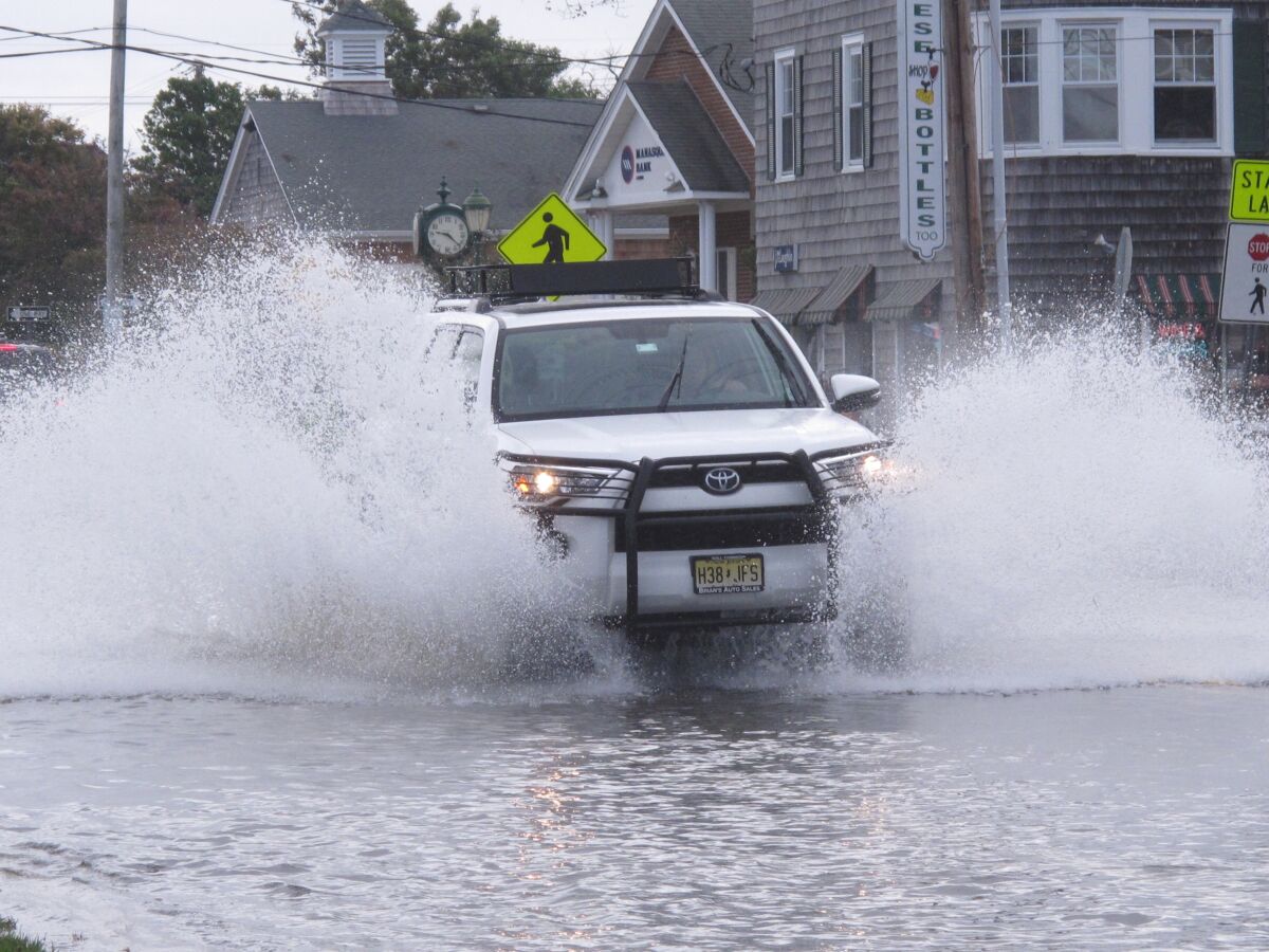 This Oct. 11, 2019 photo shows a car kicking up spray while driving through a flooded street in Bay Head, N.J. New Jersey's Department of Environmental Protection and the U.S. Army Corps of Engineers have proposed a massive $16 billion plan to address back bay flooding along the shore. But Bay Head, a wealthy, Republican-led enclave whose location at the northernmost tip of Barnegat Bay gave the town its name, feels it needs to act sooner than 2030, the earliest the ambitious project could begin construction. (AP Photo/Wayne Parry)