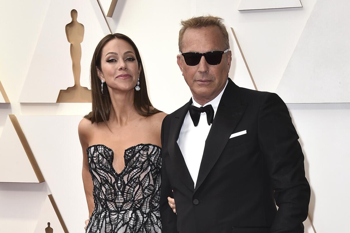 Christine Baumgartner, left, wears a black and white dress and Kevin Costner wears a black tuxedo and black sunglasses